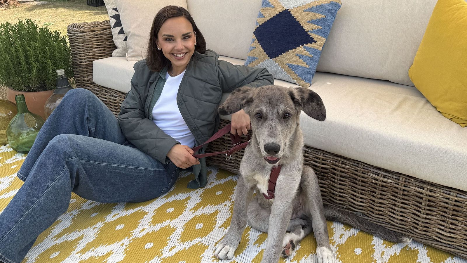 Chenoa, sonriente y con ropa casual, se sienta en un jardín junto a un perro amigable. Ambos miran a la cámara, creando una imagen cálida y natural.