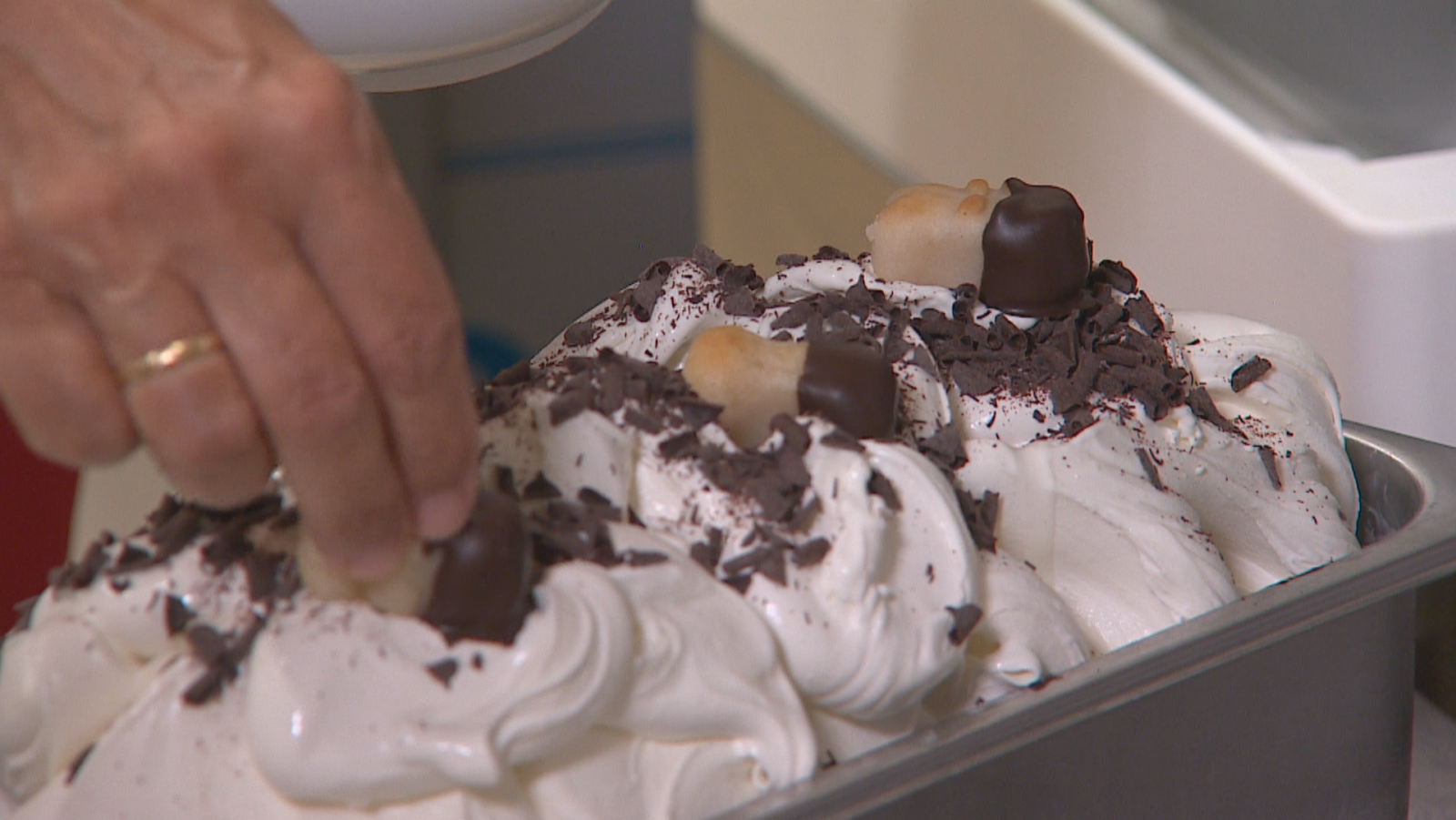Helado artesanal cremoso con virutas de chocolate y mazapanes decorativos, siendo adornado por una mano con anillo.