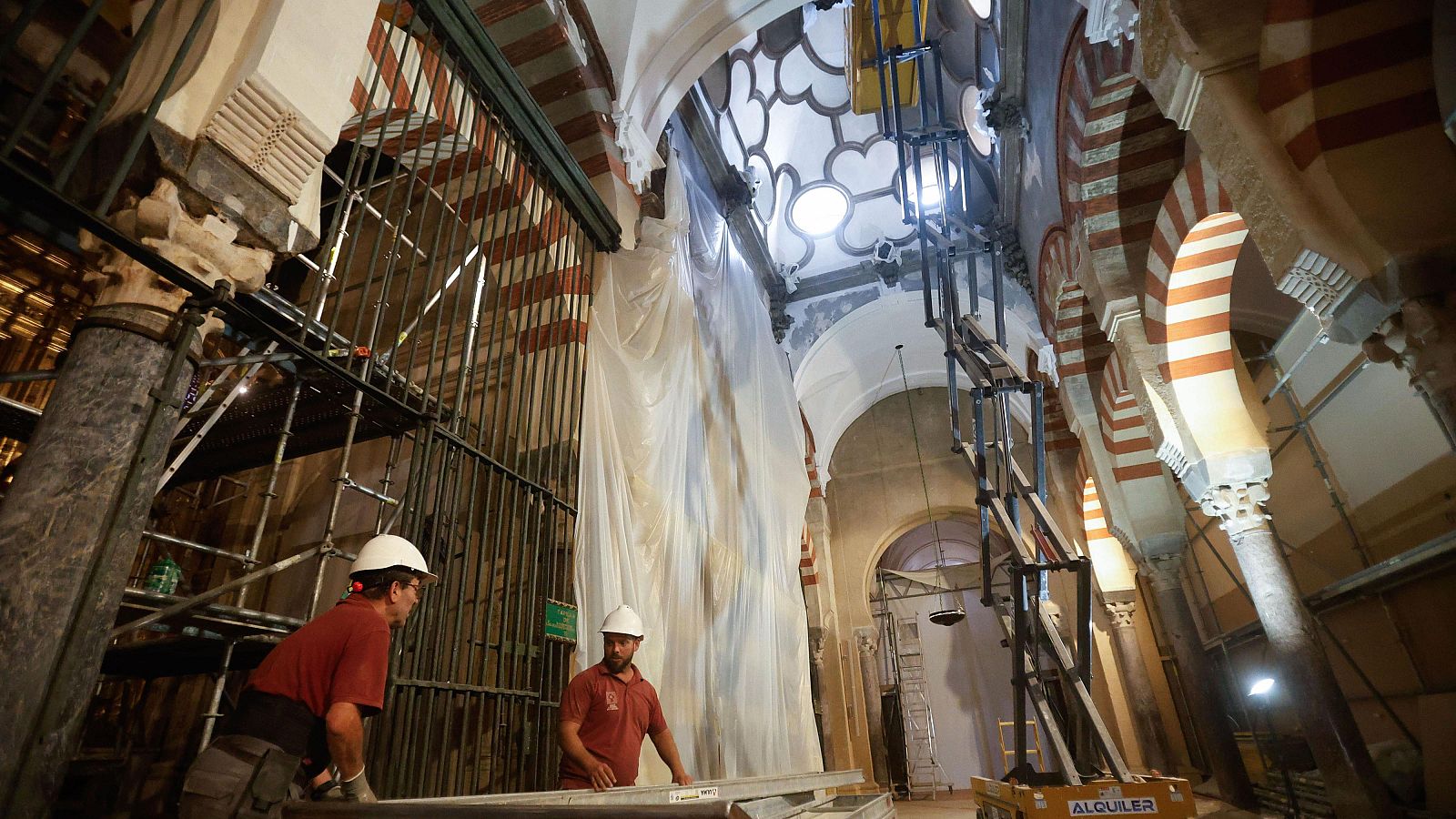 Trabajos de restauración en la Mezquita de Córdoba.  Se ven andamios, una plataforma elevadora con la palabra "ALQUILER", y dos trabajadores con cascos blancos.