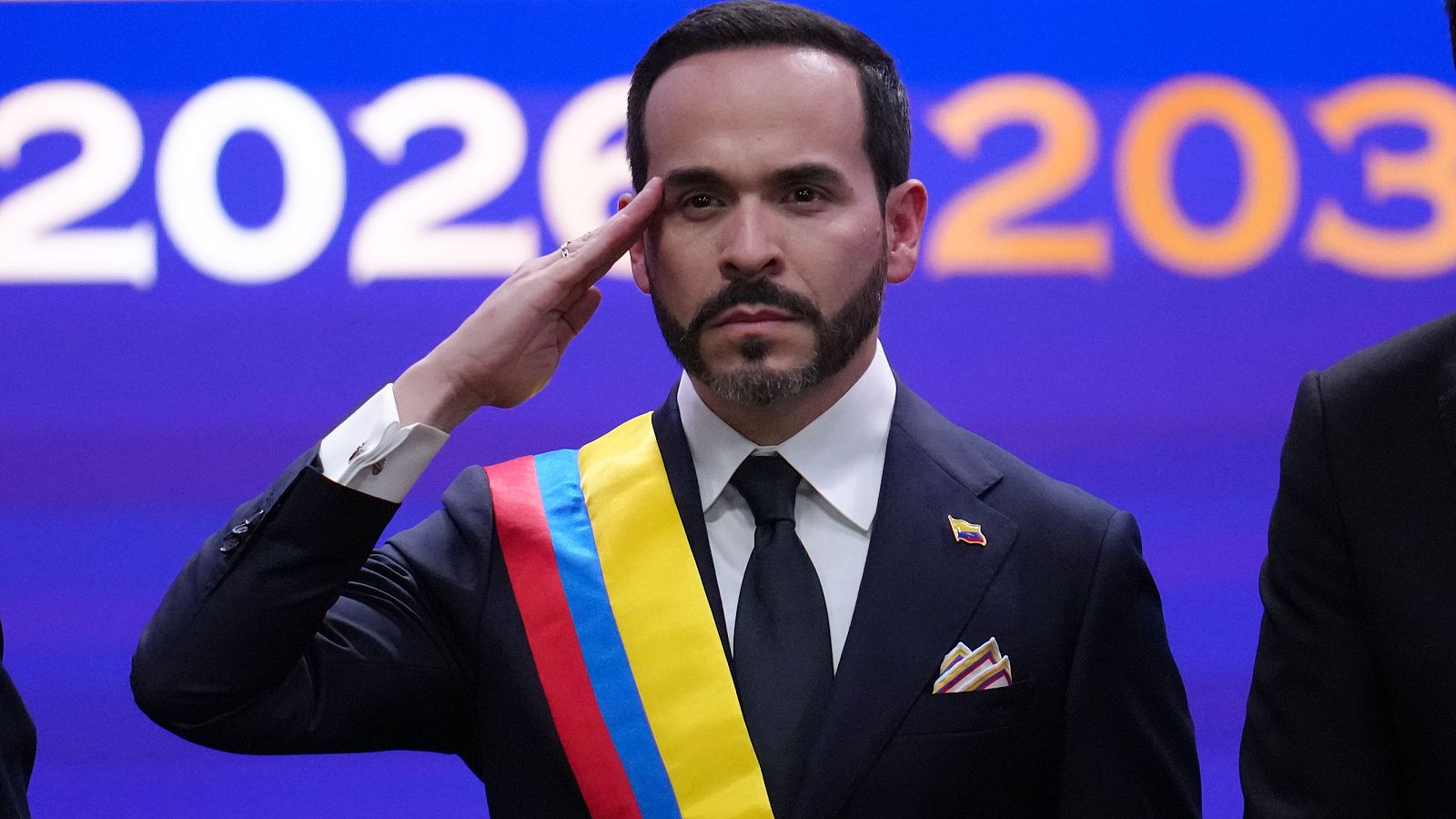 Abelardo de la Espriella, investido presidente de Colombia, posa con seriedad, luciendo traje oscuro, banda presidencial y un pin de la bandera. Su mano derecha se alza en un gesto formal.