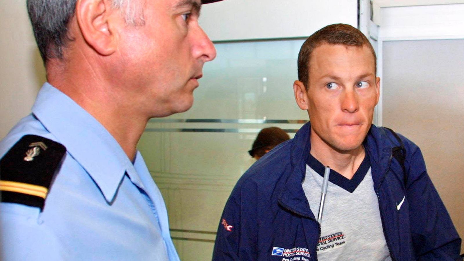 FILE PHOTO: US Postal Service team leader Lance Armstrong of the USA looking at a French gendarme before boarding for the transfer stage of the Tour de France cycling race