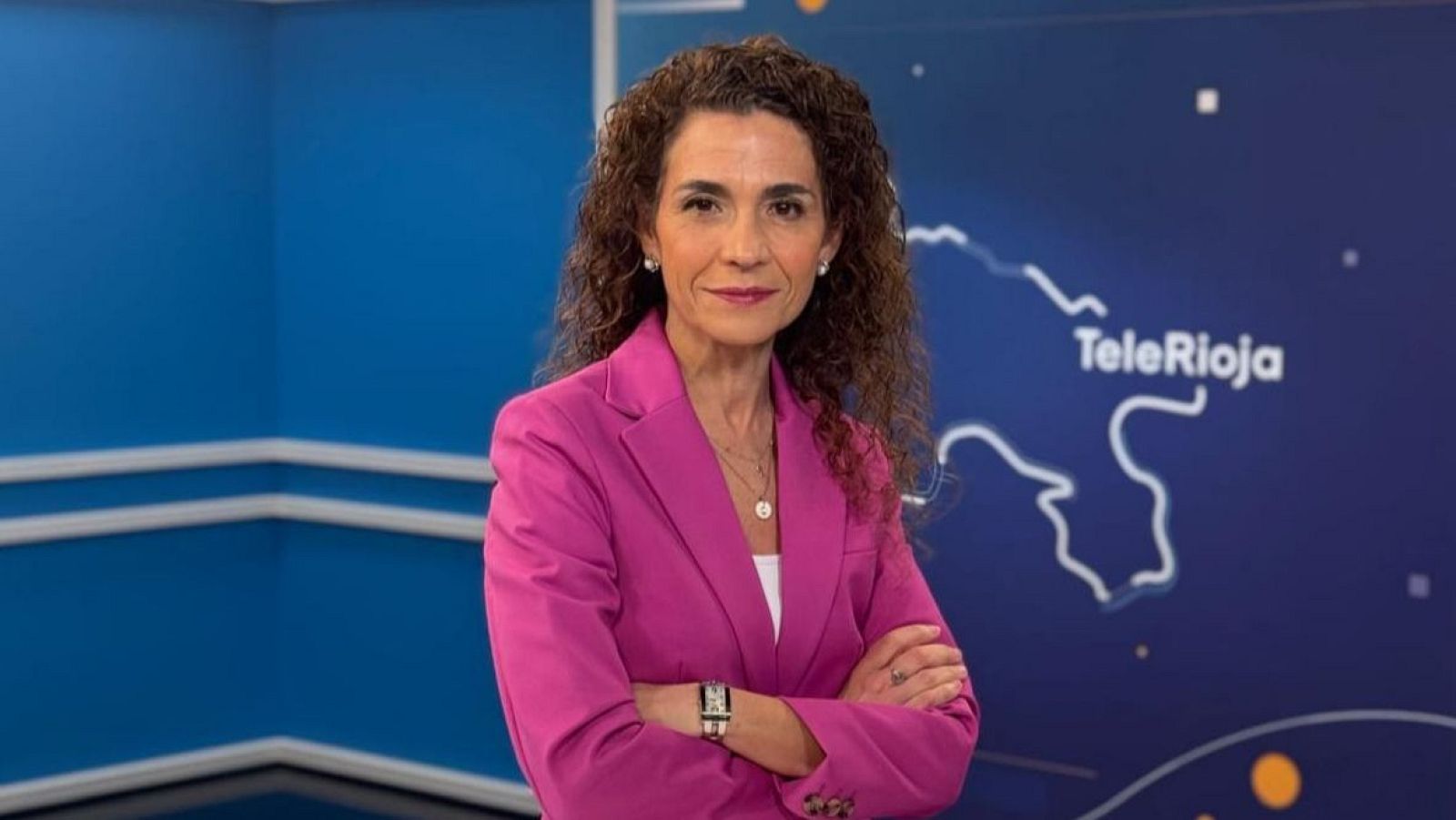 Concepción Aquesolo, directora de RTVE La Rioja, en un retrato profesional con americana fucsia y fondo de estudio con logo "TeleRioja".