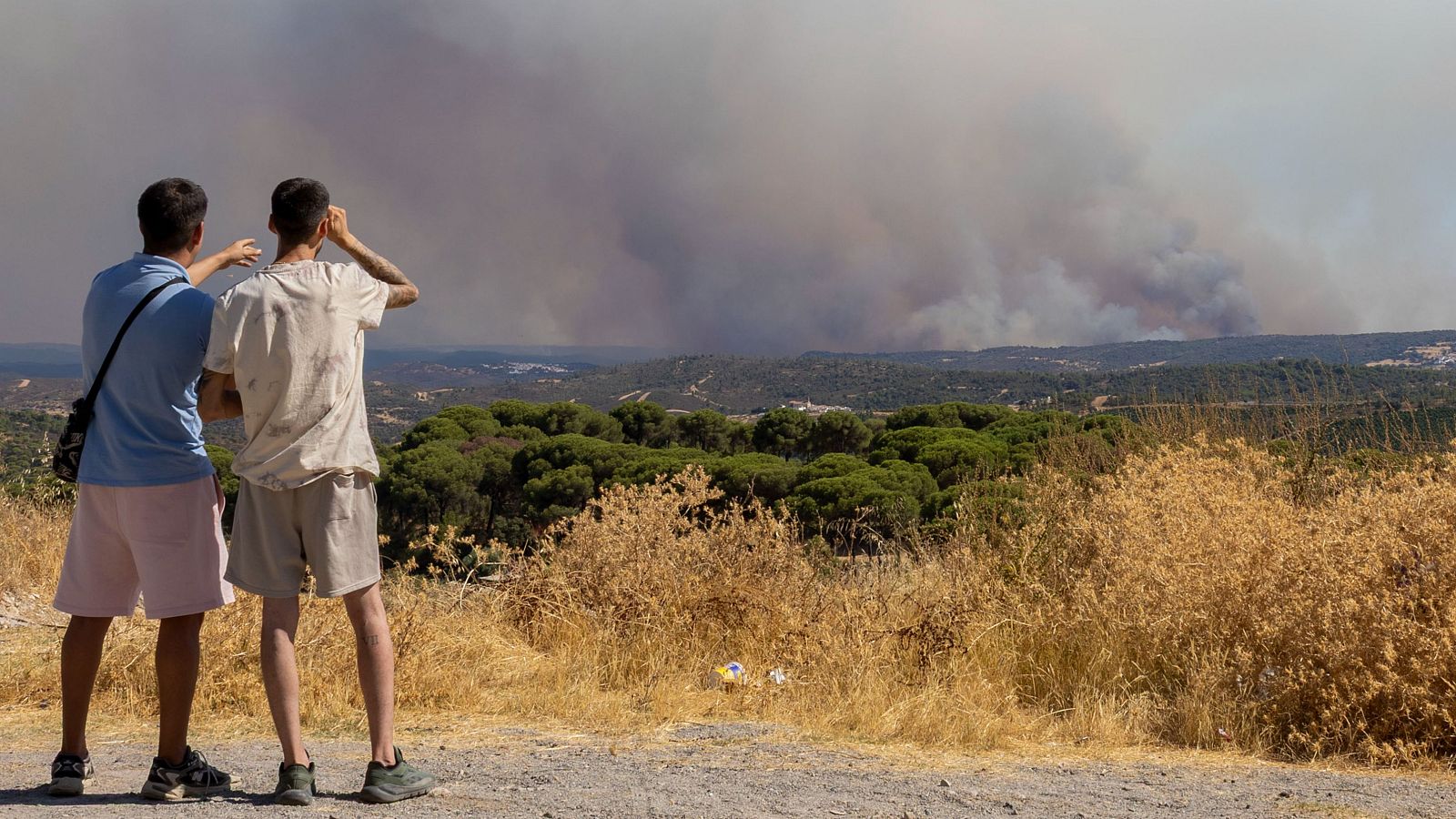 Dos jóvenes observan desde un mirador de las minas de Río Tinto la imponente columna de humo y el avance del fuego del incendio de Niebla en Huelva