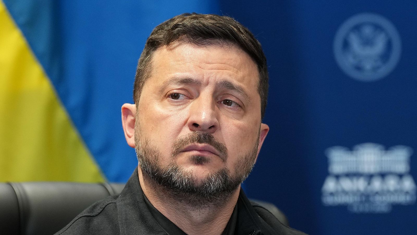 Primer plano de Volodímir Zelenski con expresión seria, bandera de Ucrania y texto "ANKARA" al fondo.