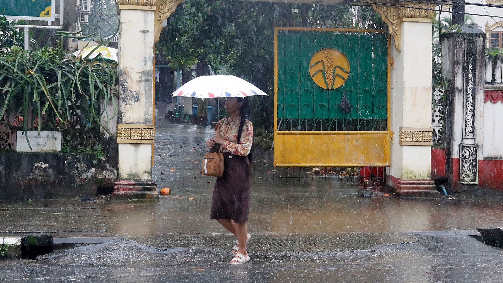 Una mujer camina bajo la lluvia en Yangón, Myanmar, país que se enfrenta al riesgo de fenómenos meteorológicos extremos por El Niño combinado con el monzón del suroeste.