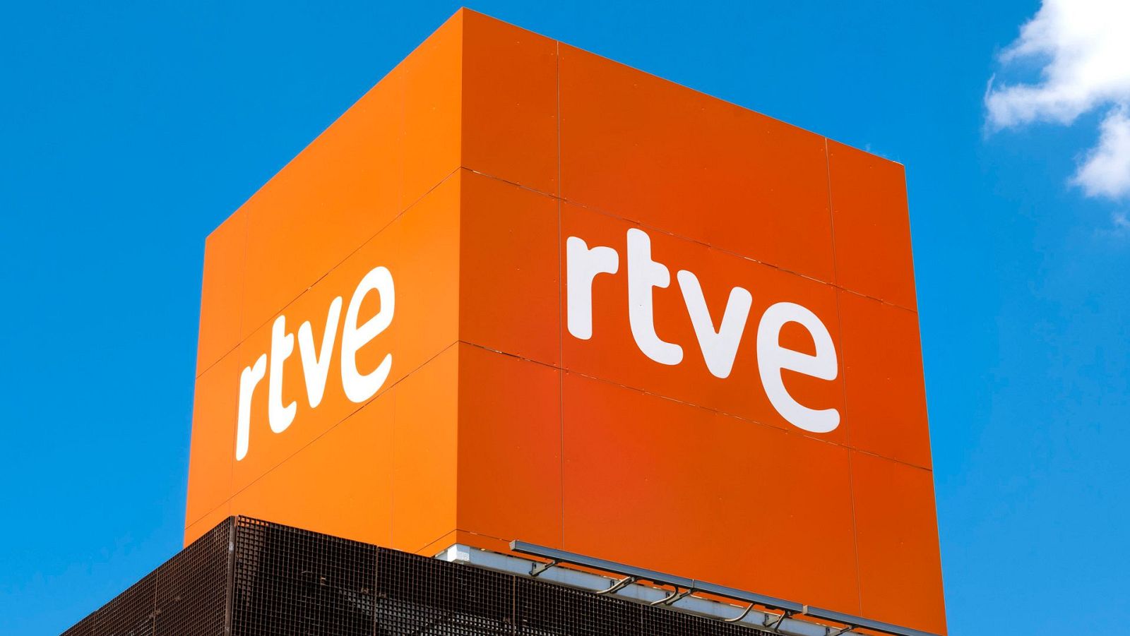 Cubo naranja con logo "rtve" en la sede de RTVE en Torrespaña, Madrid, contra un cielo azul.