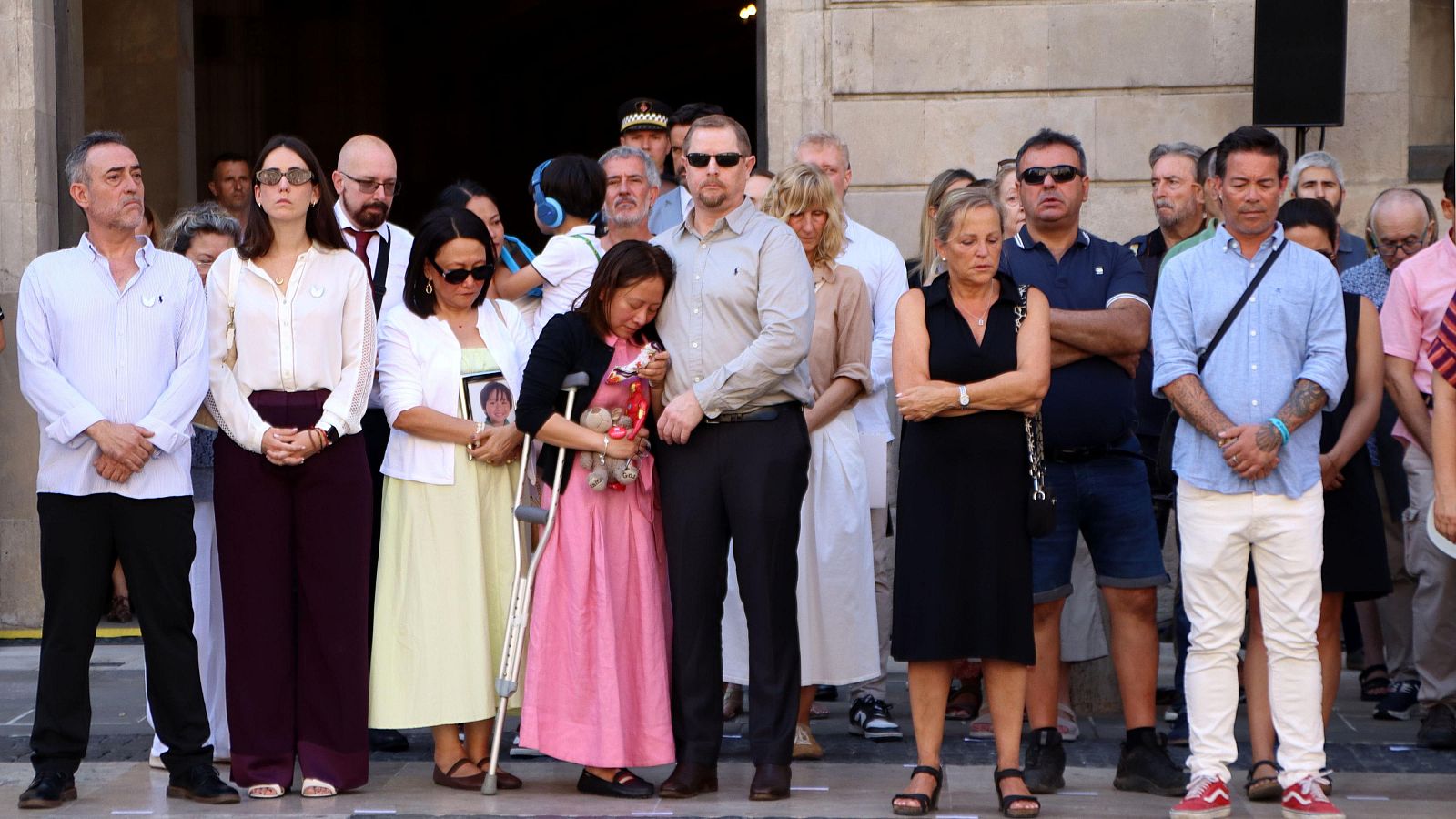 Familiars de les víctimes del 17-A en un minut de silenci a la Plaça Sant Jaume, Barcelona. Són visibles gestos de dol, una fotografia d'un nen i un os de peluix.