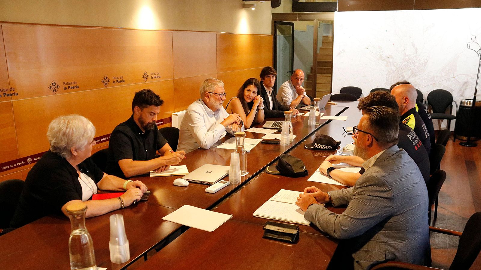 Reunió al Palau de la Paeria amb Miquel Pueyo i agents de policia, discutint temes municipals al voltant d'una taula amb portàtils i documents.