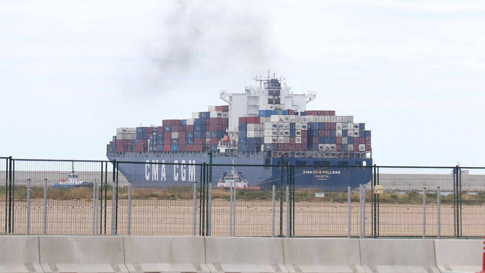 El vaixell portacontenidors "CMA CGM PELLEAS" (VALLETTA) navega amb l'ajuda de remolcadors, carregat de contenidors i amb fum sortint de la xemeneia, sota un cel ennuvolat.