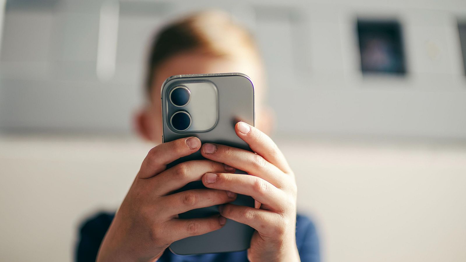 Mans joves subjecten un telèfon mòbil gris fosc amb un mòdul de càmera doble a la part posterior. Els polzes interactuen amb la pantalla.