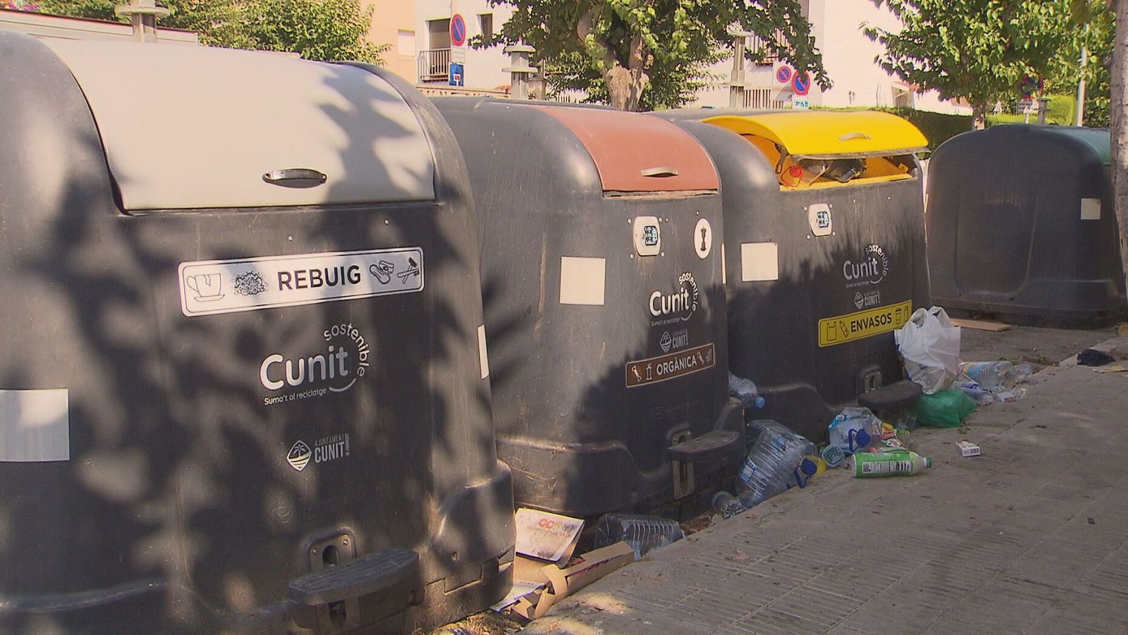 Contenedores de reciclaje en Cunit, Costa Daurada, con basura esparcida. Se distinguen los tipos "REBUIG", "ORGÀNICA" y "ENVASOS".