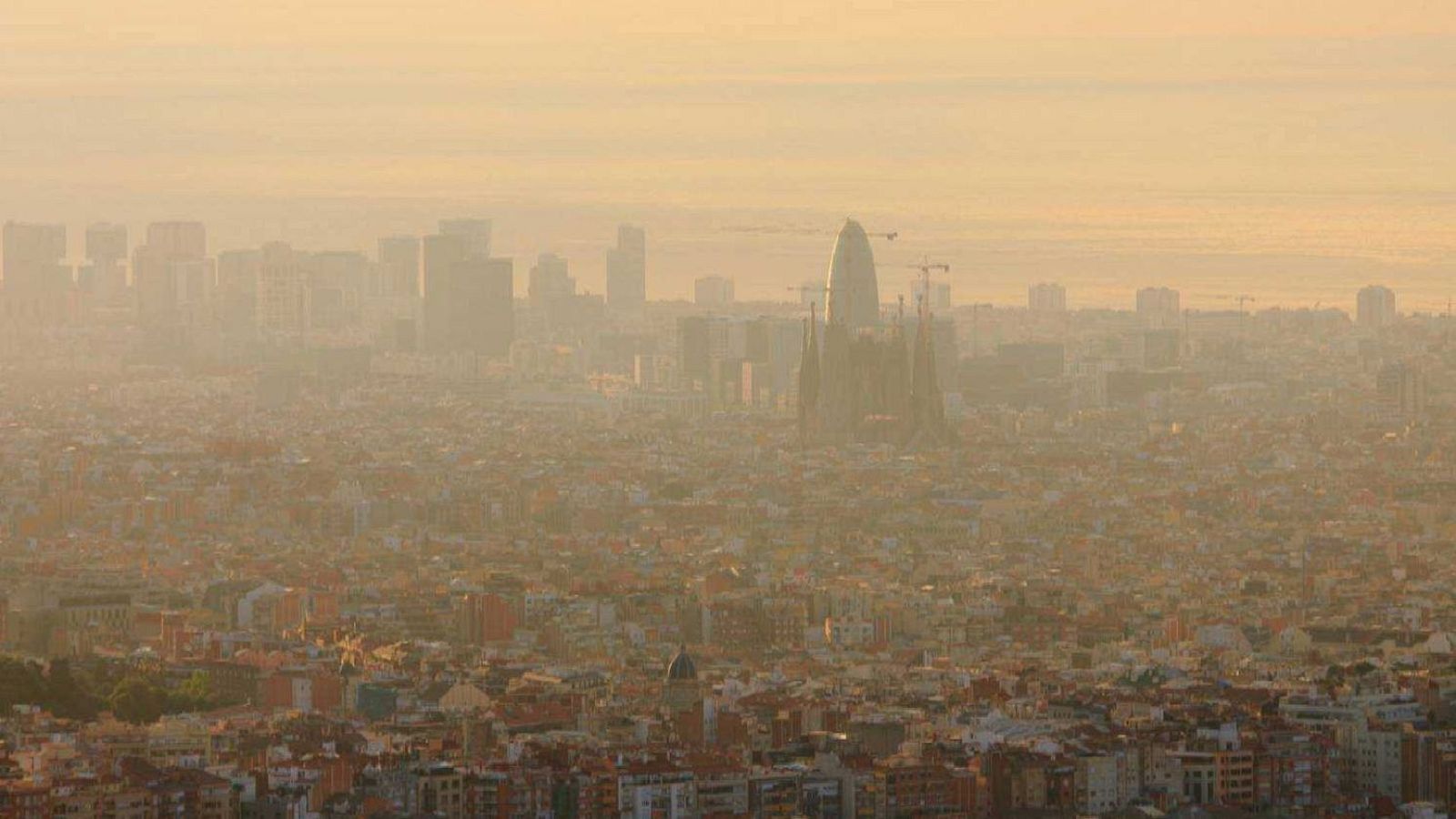 Vista aèria de Barcelona amb boira de contaminació, destacant la Sagrada Família i la Torre Glòries entre edificis.