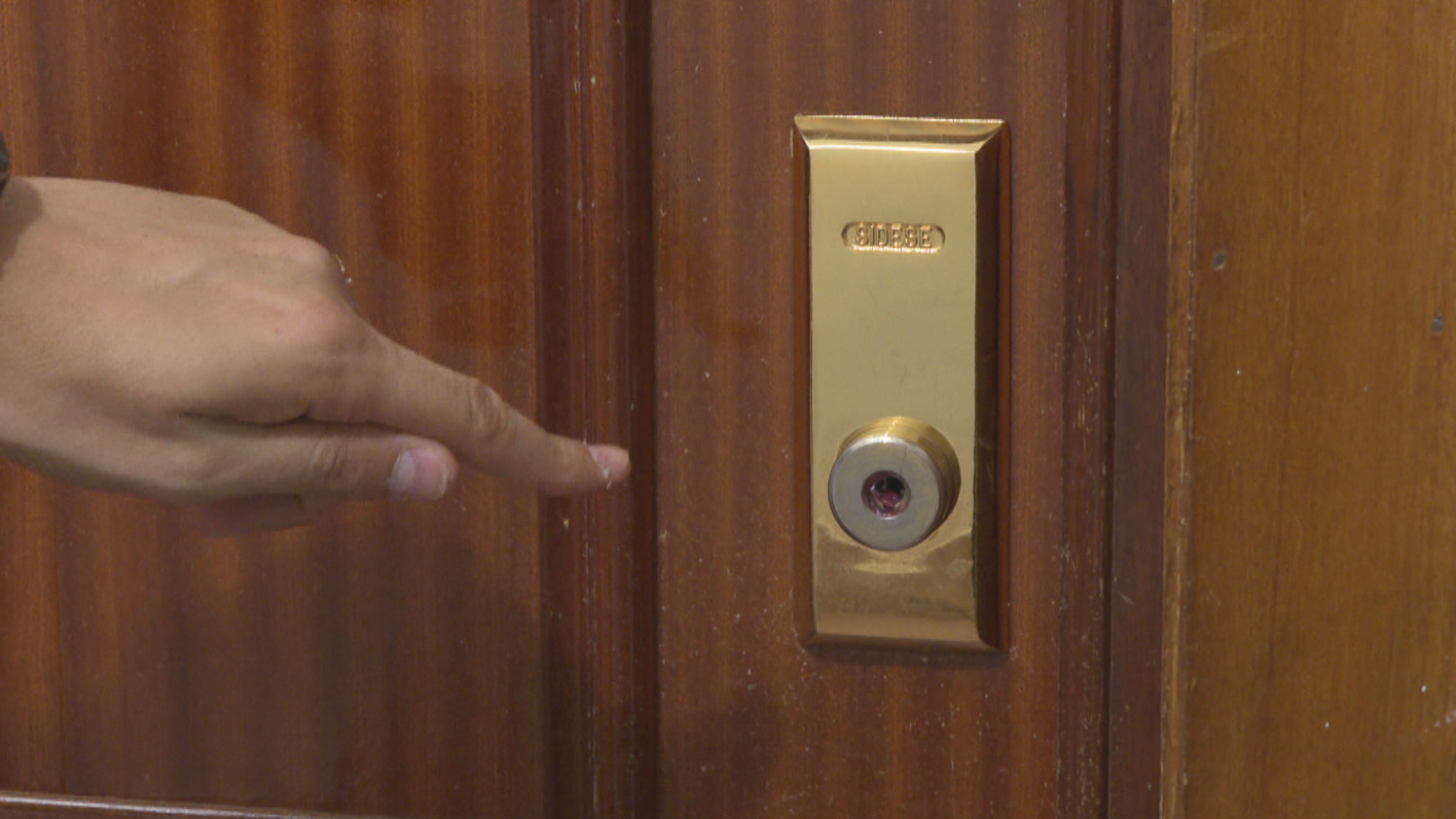 Primer plano de una cerradura "CISA" en una puerta de madera, con una mano señalando una sustancia grasa adherida, indicando un método de robo.
