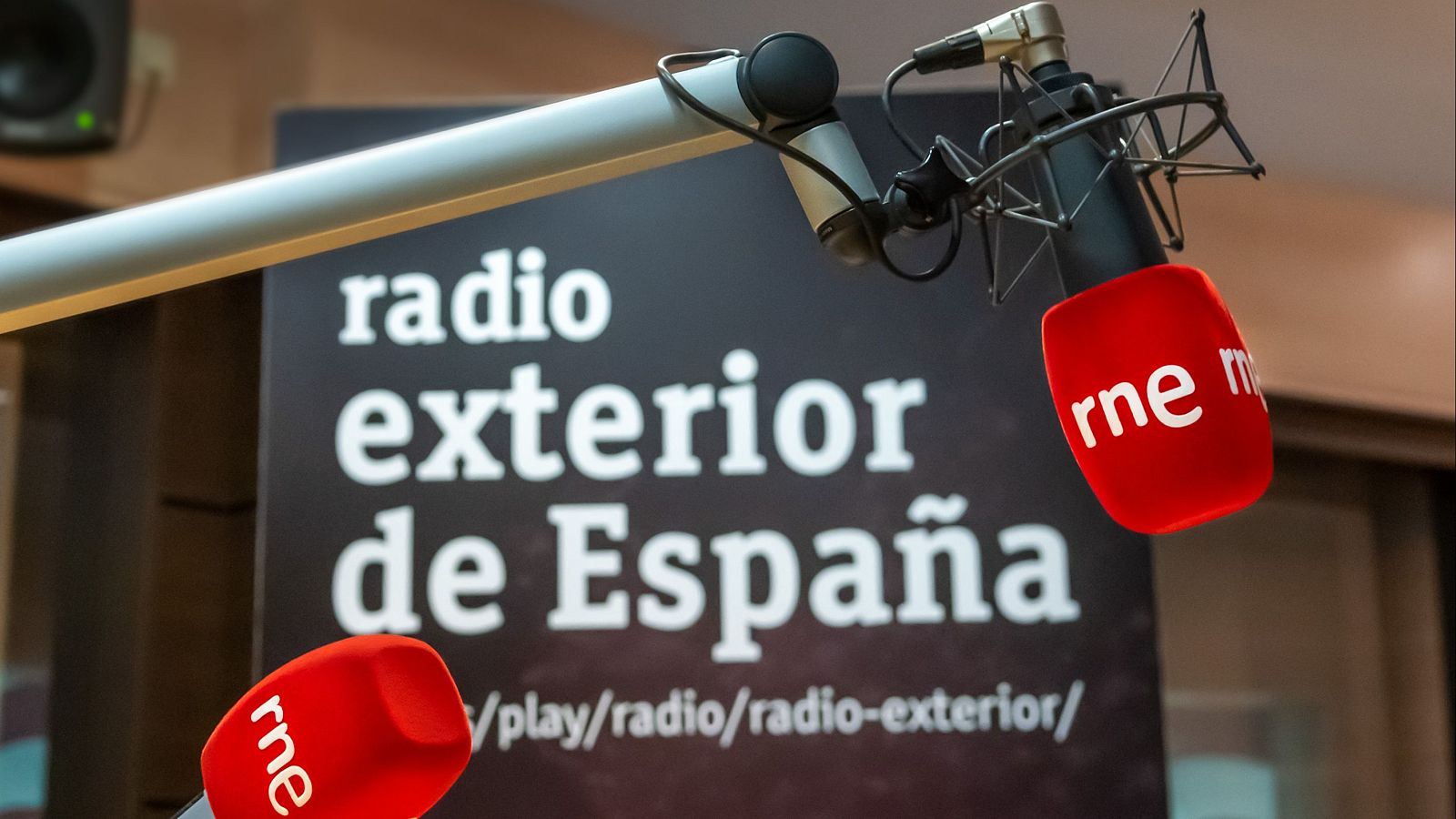 Micrófono profesional con pantalla antiviento roja "rne" en un estudio de radio, con el cartel "radio exterior de España" al fondo.