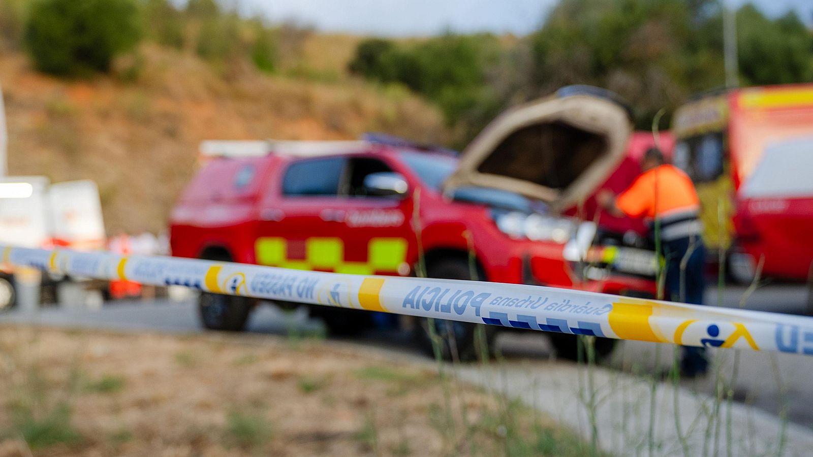 Bombers treballant en un vehicle d'emergències amb el capó obert, amb una cinta de "POLICIA" al davant, en un entorn natural.