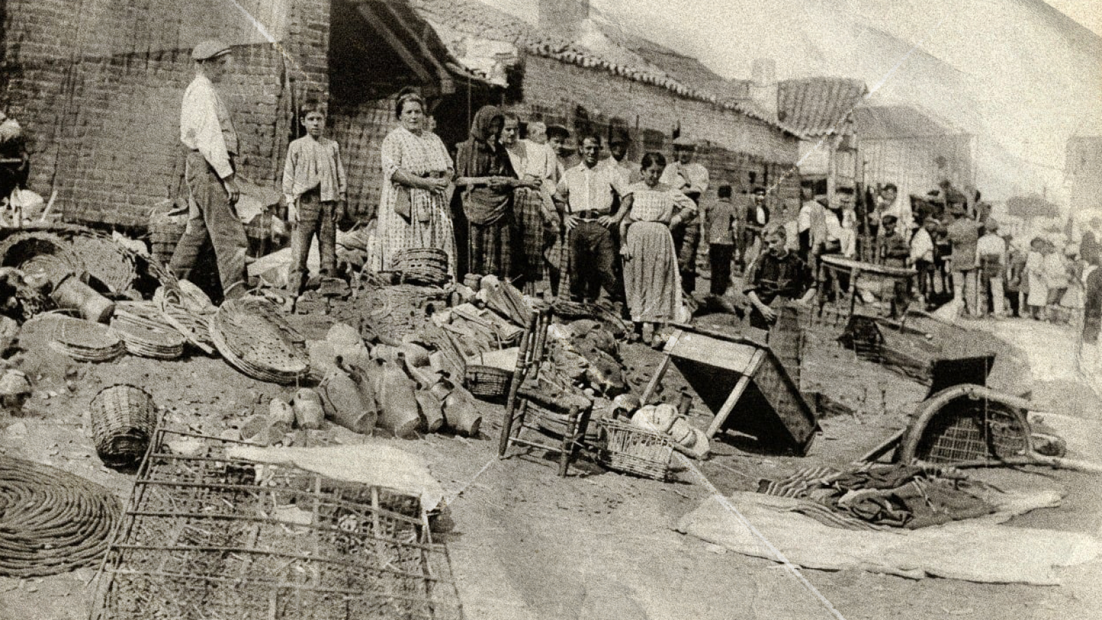 Vecinos observan los destrozos en una calle de un pueblo español tras una riada de 1926, con escombros y edificios dañados.
