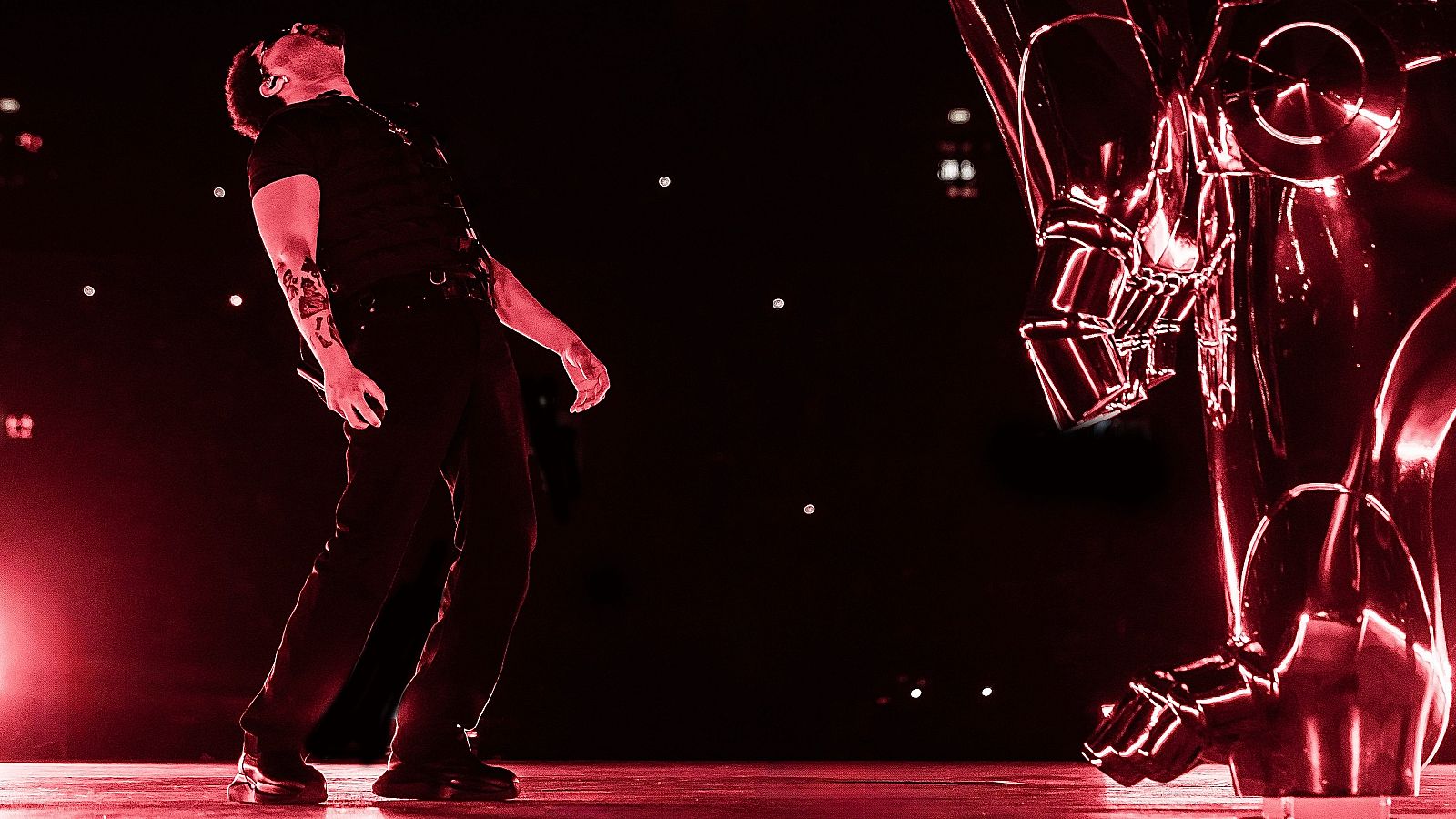 The Weeknd canta apasionadamente en un concierto en Londres, bajo una potente luz roja, junto a una escultura futurista en el escenario.