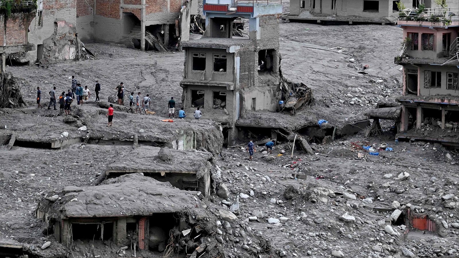 Vista aérea de Trishuli, Nepal, tras una riada masiva. Edificios destruidos y cubiertos de lodo. Personas inspeccionan la zona devastada.