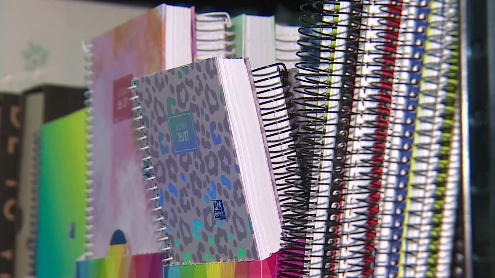 Primer plano de agendas y cuadernos de espiral con el texto "26/27" en una agenda de leopardo. Variedad de colores en espirales.