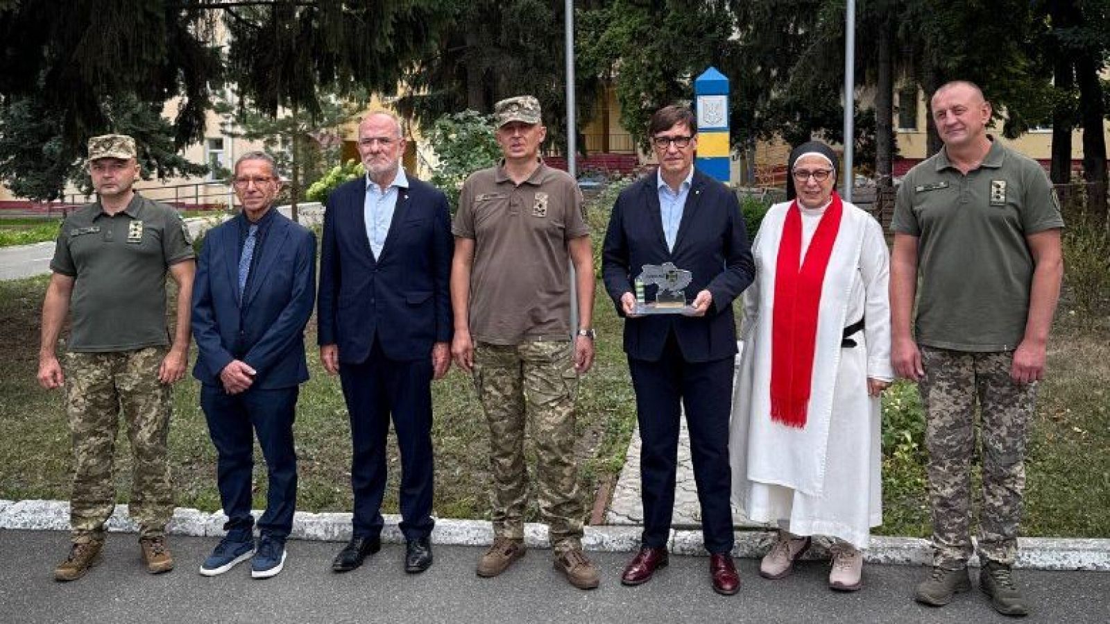 Salvador Illa y Sor Lucía Caram posan con militares ucranianos frente a un poste con franjas azules y amarillas.