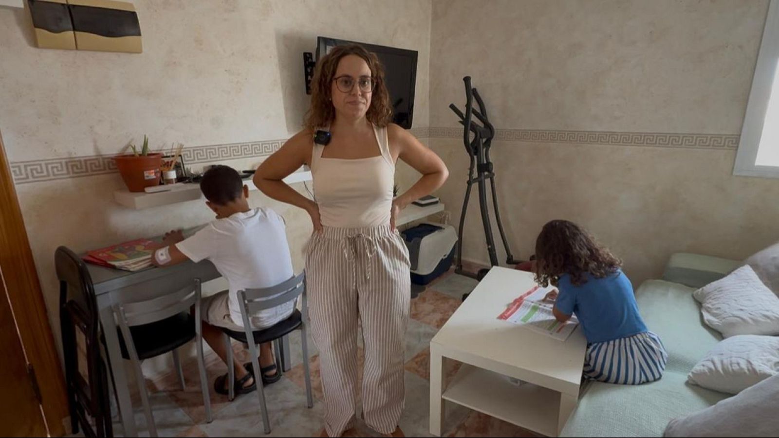 Aurora Botello y sus hijos en un salón luminoso, a dos días del inicio del curso escolar. Ella posa, mientras los niños estudian en un escritorio y un sofá.