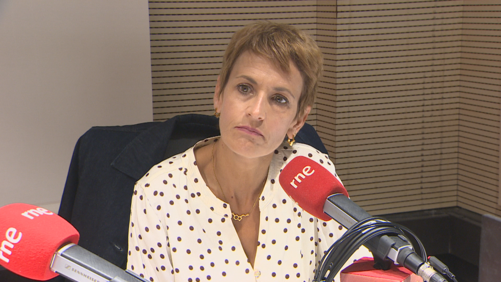 Maria Chivite, Presidenta del Gobierno de Navarra, en un estudio de radio, con micrófonos de RNE y fondo de paneles acústicos.