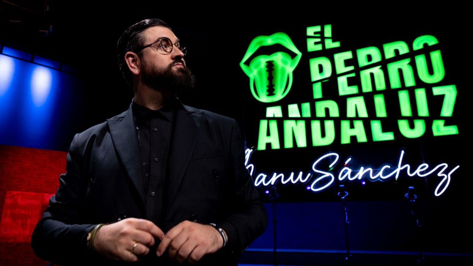 Manu Sánchez, presentador, posa en un plató con el letrero de neón "EL PERRO ANDALUZ" y su nombre en blanco cursivo.