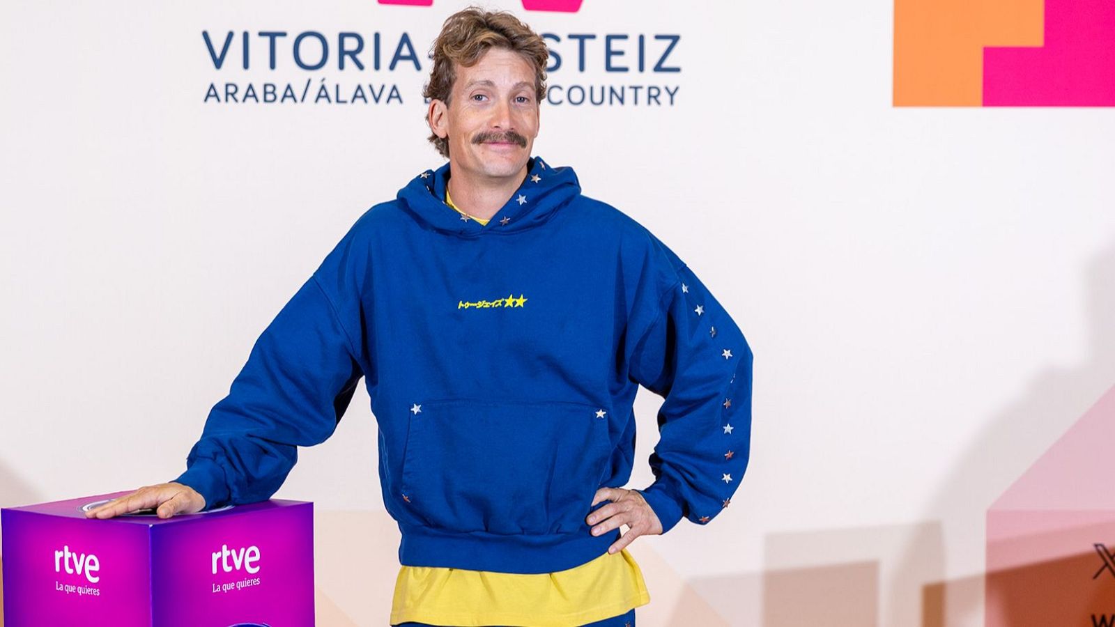 Grison, con sudadera azul y estrellas, posa junto a una caja morada de RTVE en Vitoria-Gasteiz.
