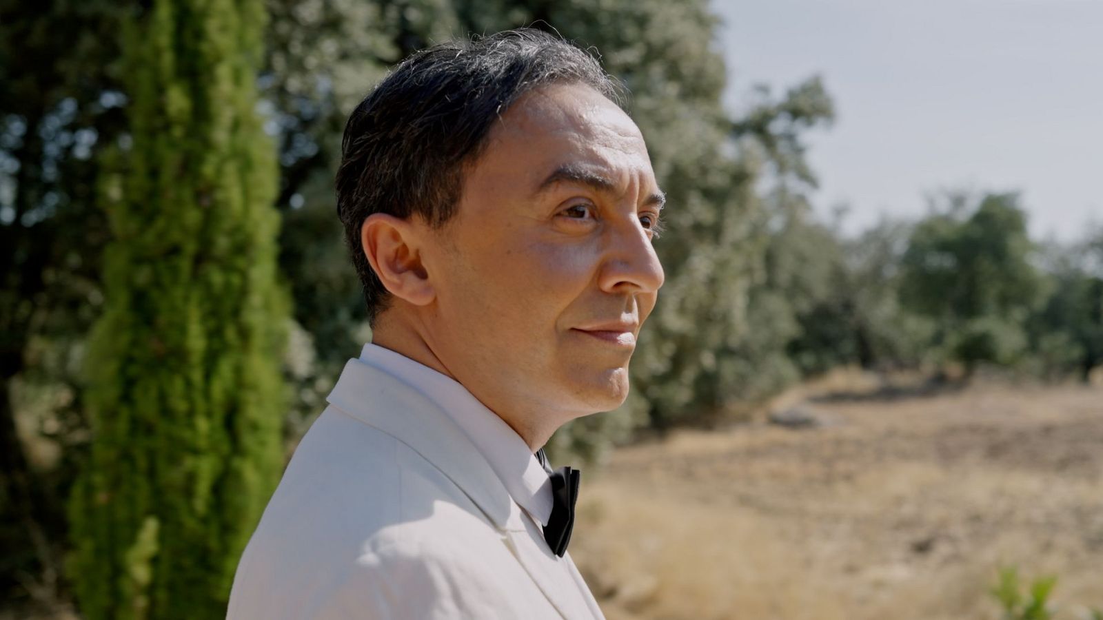Ángel Ruiz como Federico García Lorca, de perfil, con traje blanco y pajarita negra, ante un paisaje natural.
