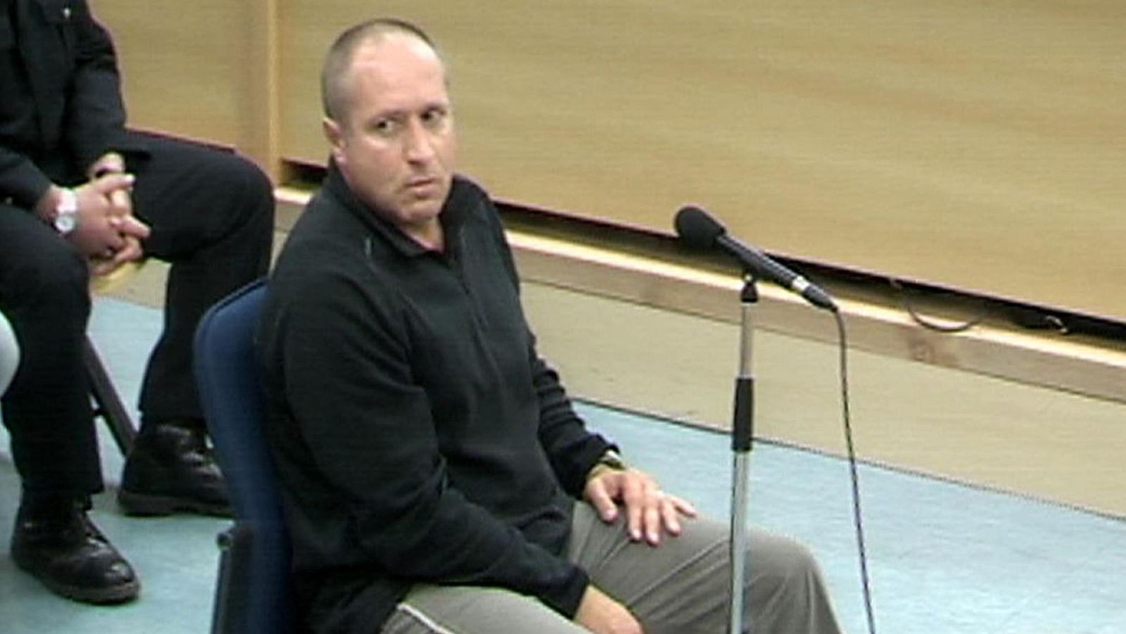 Henri Parot, con sudadera oscura y reloj dorado, en una sala de audiencias con un micrófono frente a él.