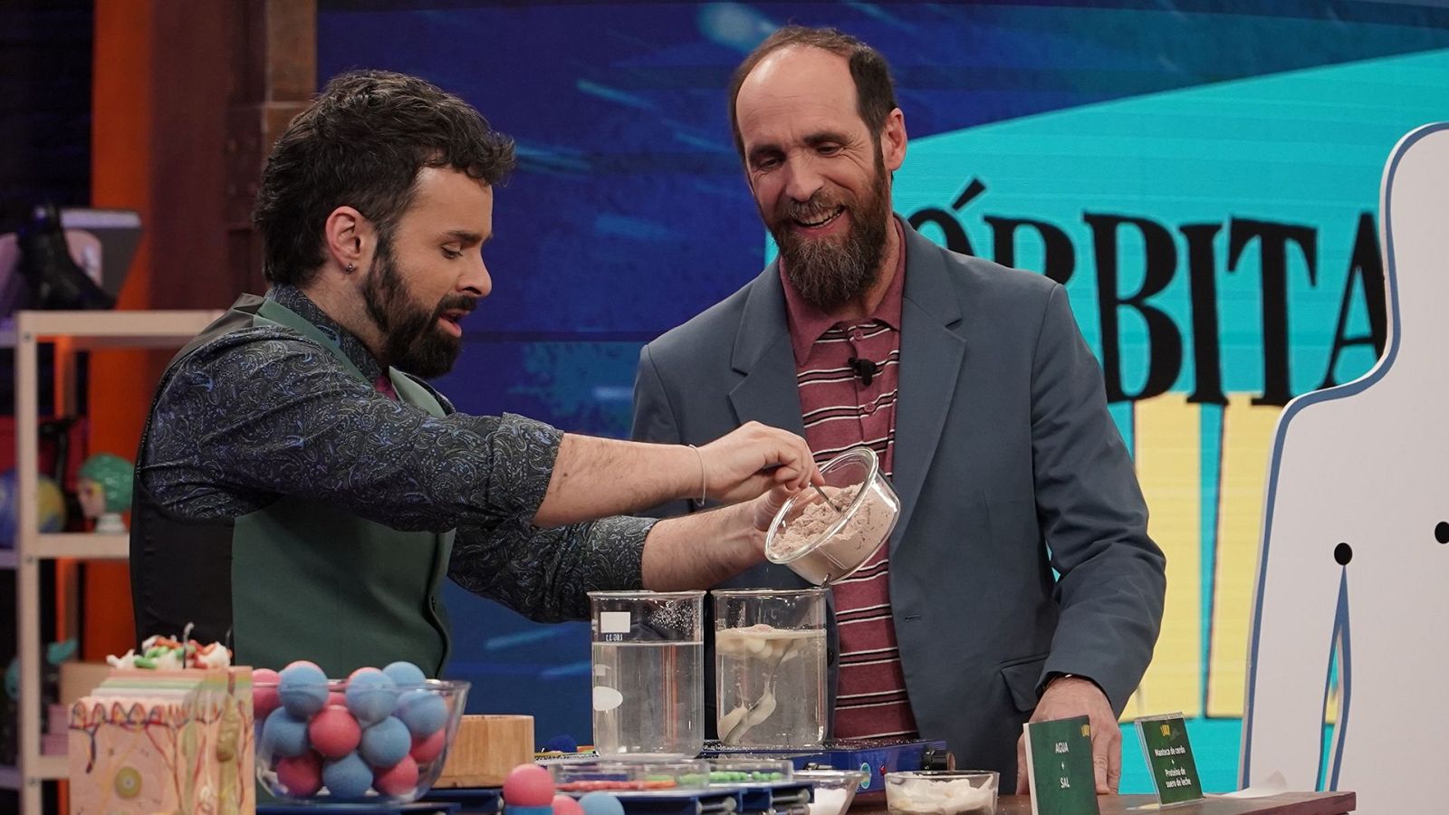 Ricardo Moure y Eduardo Sáenz de Cabezón realizan un experimento científico en "Órbita Laika", rodeados de material de laboratorio y un modelo de tejido biológico.