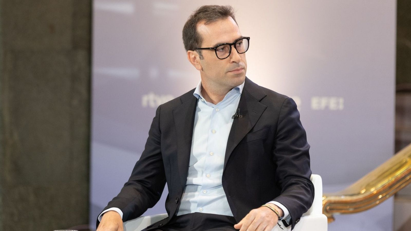 Carlos Cuerpo, Ministro de Economía, con gafas y traje, en una entrevista con logos de RTVE y EFE al fondo.