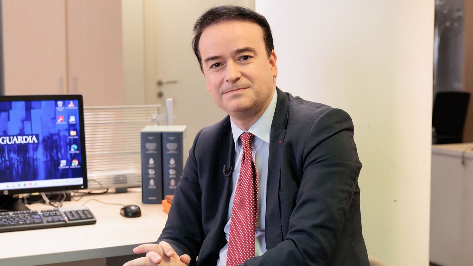 Iván Redondo, con traje y corbata, sentado en una mesa con un monitor que muestra "GUARDIA".