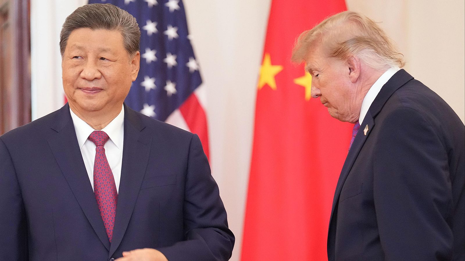 Xi Jinping y Donald Trump en un encuentro formal. Xi viste traje azul marino con corbata granate; Trump, traje azul marino con corbata morada. Se ven las banderas de EE.UU. y China.