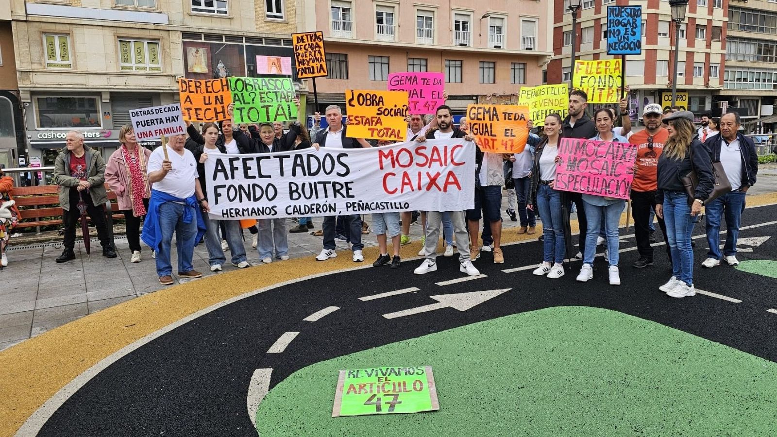 Grupo de manifestantes concentrados frente a un edificio de viviendas en la calle Hermanos Calderón, Cantabria, sosteniendo pancartas con lemas por el derecho a la vivienda y contra los desahucios.