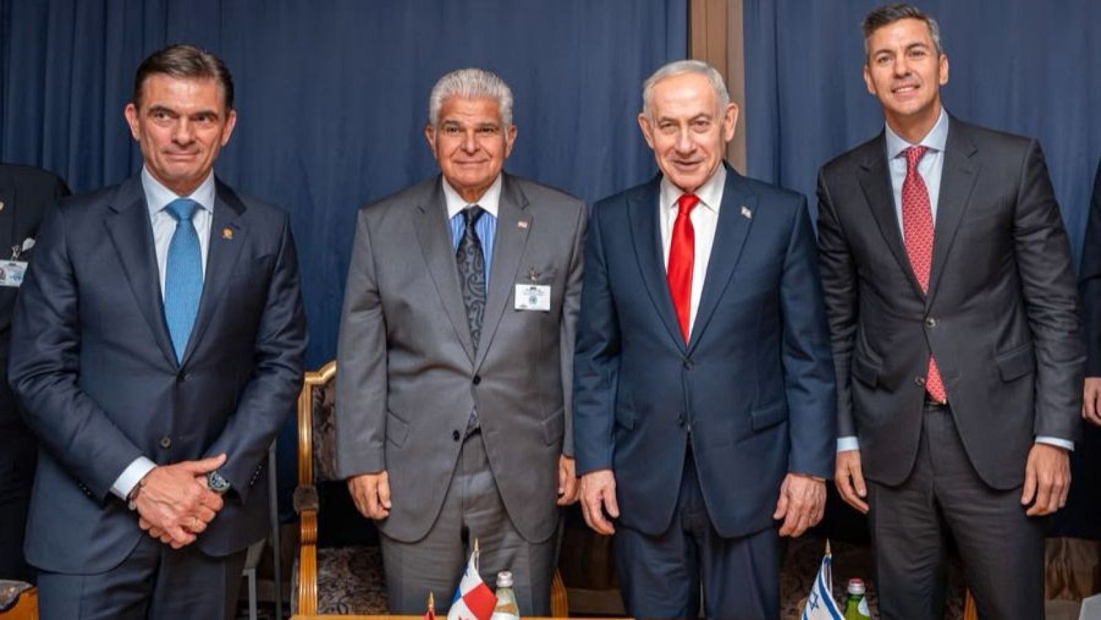 Rodrigo Paz, José Raúl Mulino, Benjamin Netanyahu y Santiago Peña posan en un encuentro diplomático. Se aprecian banderas de Israel y Panamá, y una botella sobre una mesa.