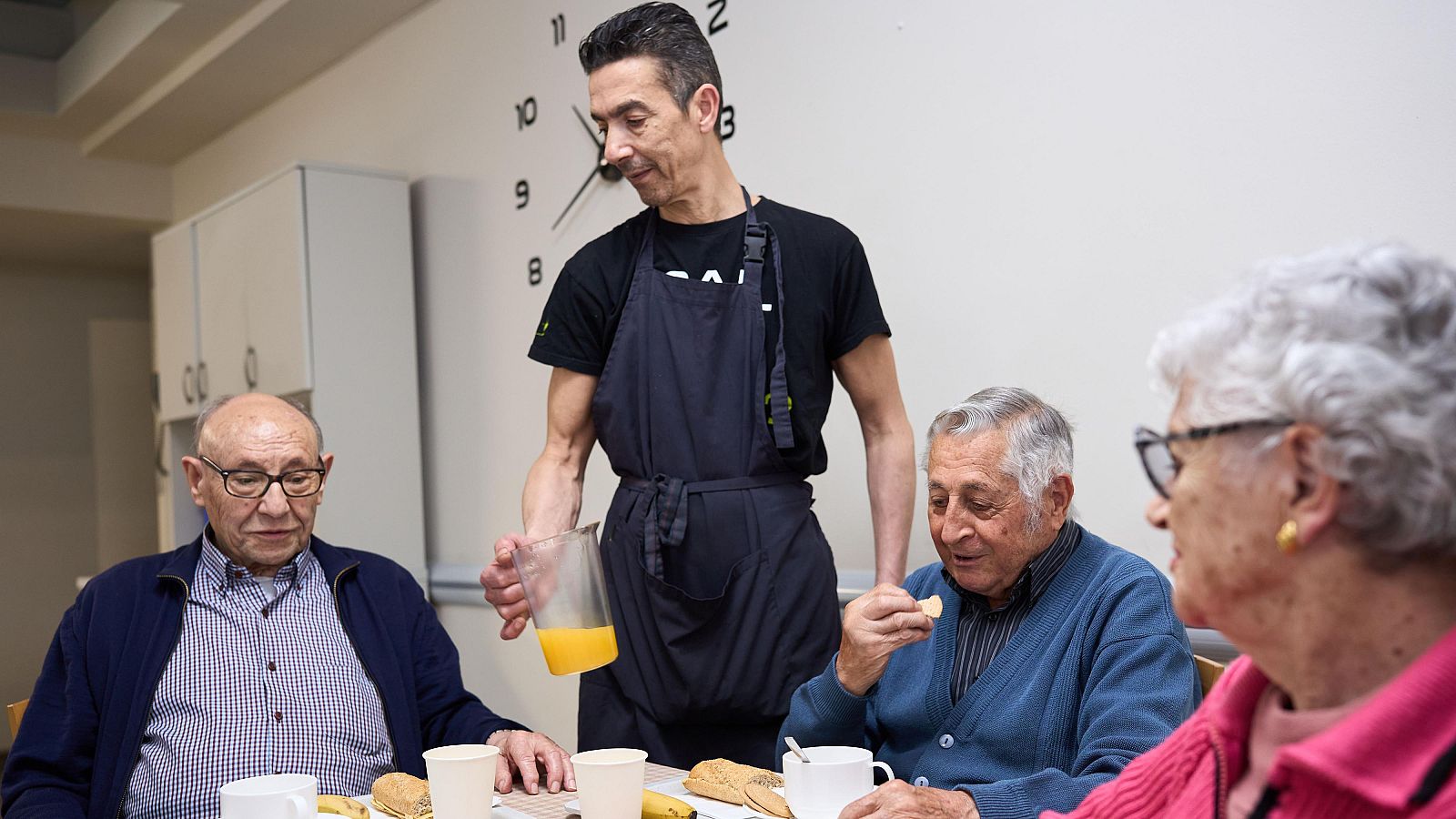 Hombre sirviendo el desayuno a residentes mayores en una residencia de ancianos