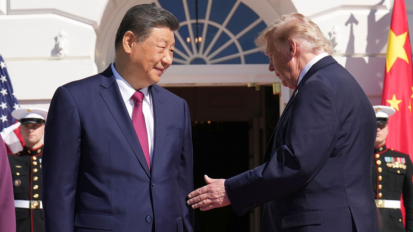 Xi Jinping y Donald Trump se saludan frente a la Casa Blanca, con las banderas de China y EE.UU. al fondo. Ambos visten trajes formales.