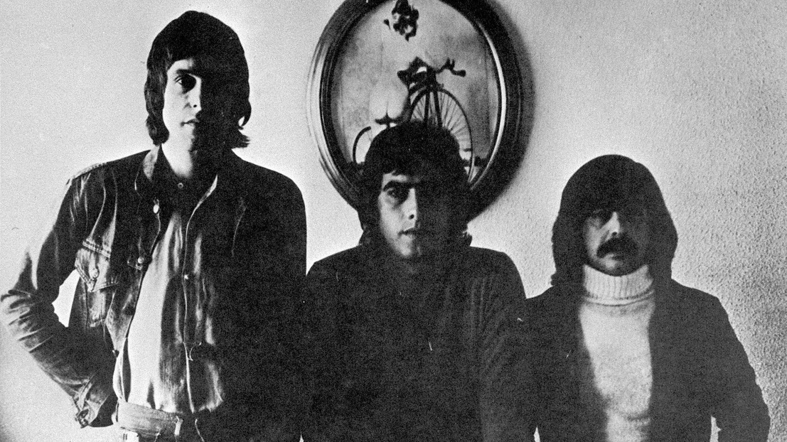 Retrato en blanco y negro de los integrantes de Triana: Eduardo Rodríguez Rodway, Jesús de la Rosa Luque y Juan José Palacios "Tele", con peinados largos y vestimenta de los 70.