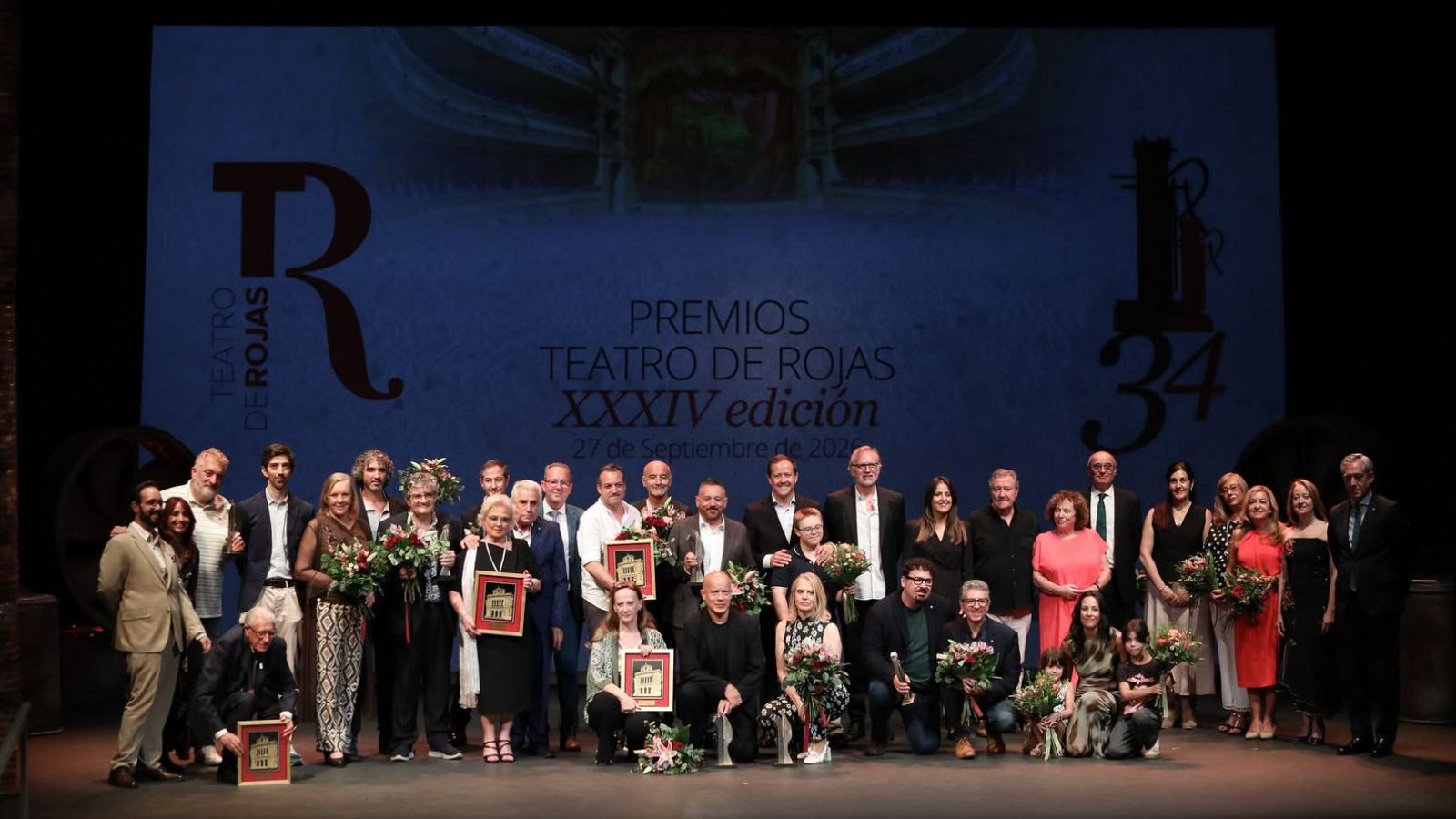 Grupo de galardonados sonrientes en el escenario del Teatro de Rojas, celebrando la XXXIV edición el 27 de septiembre de 2020, con placas y flores.
