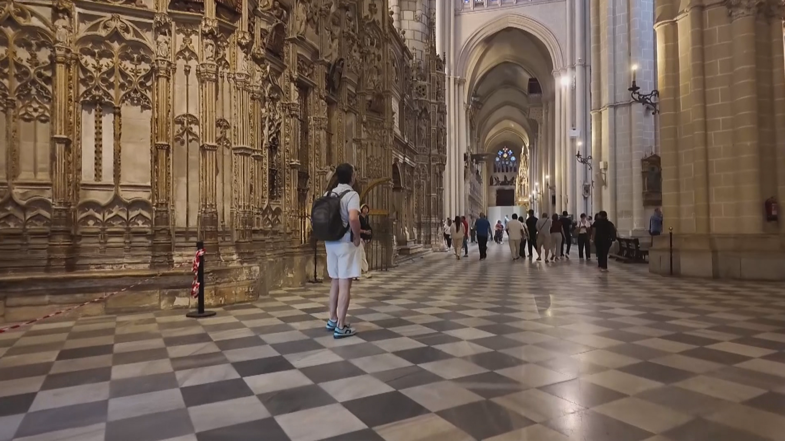 Un visitante con mochila contempla la imponente pared tallada de la Catedral de Toledo, rodeado de columnas góticas y bóvedas iluminadas.