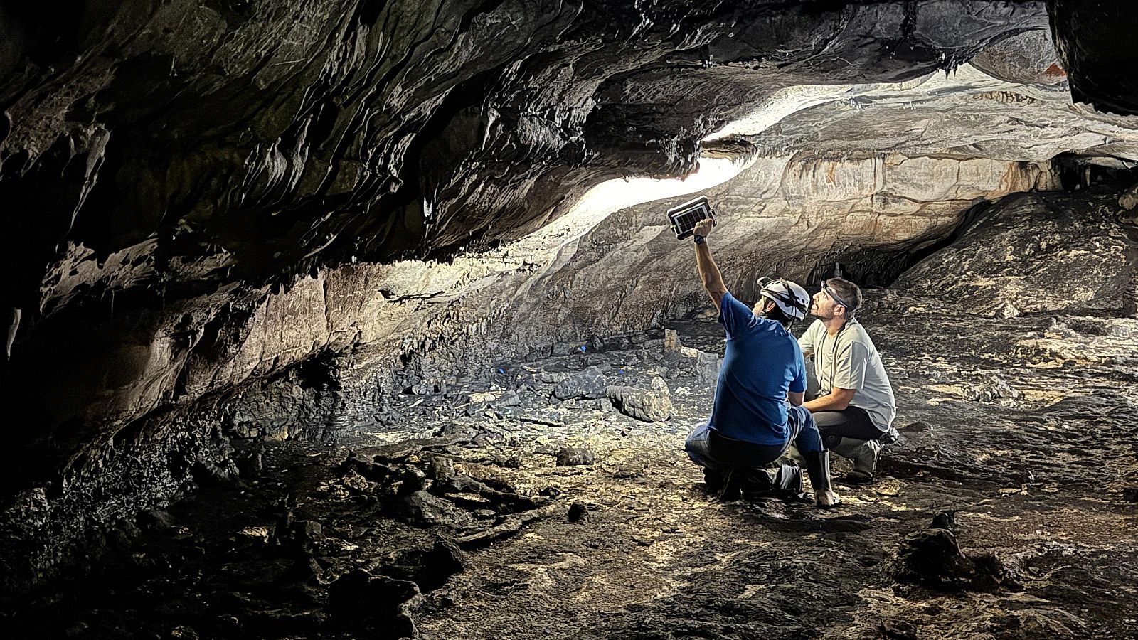 Dos arqueólogos documentan con un dispositivo electrónico el techo rocoso de la Cova Dones en Millares, Valencia, bajo una intensa luz que ilumina la cavidad.