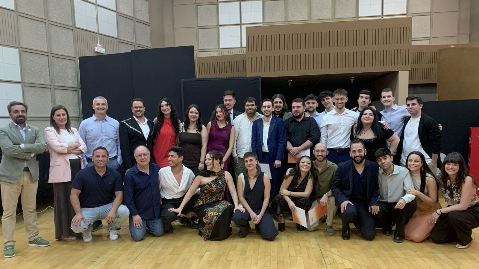 Fotografía de grupo de graduados en un auditorio, con Ignacio Elguero de RTVE presente. Los asistentes sostienen diplomas naranjas.