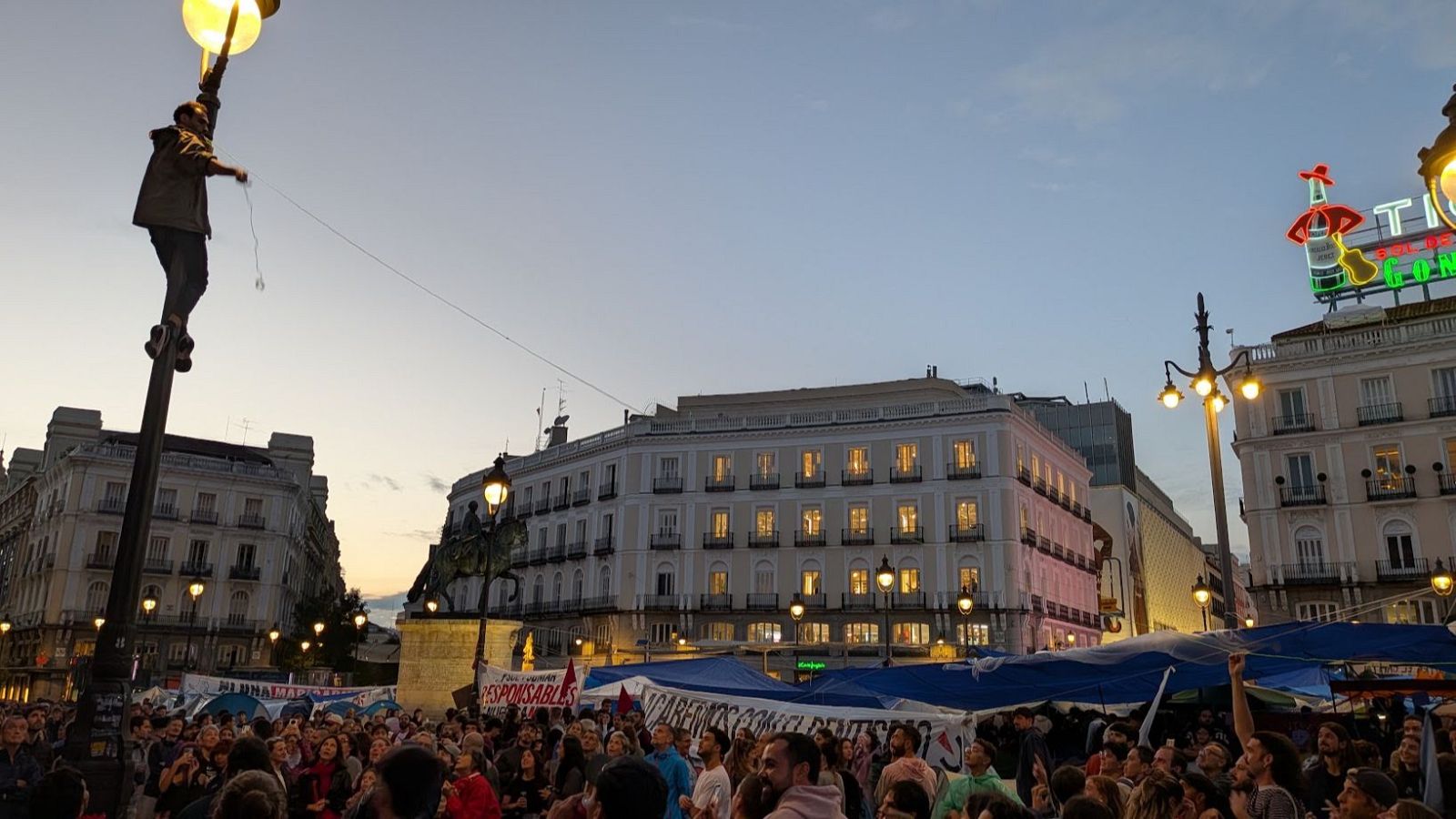 Un hombre coloca un toldo para proteger la acampada de la Puerta del Sol de la lluvia