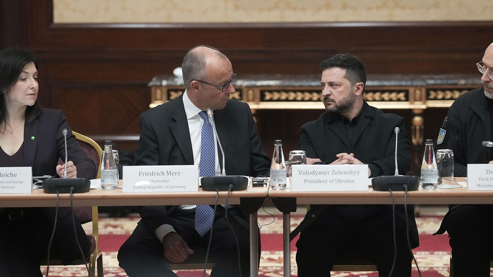 Reunión diplomática formal con Friedrich Merz y Volodímir Zelenski sentados en una mesa con micrófonos y carteles identificativos.