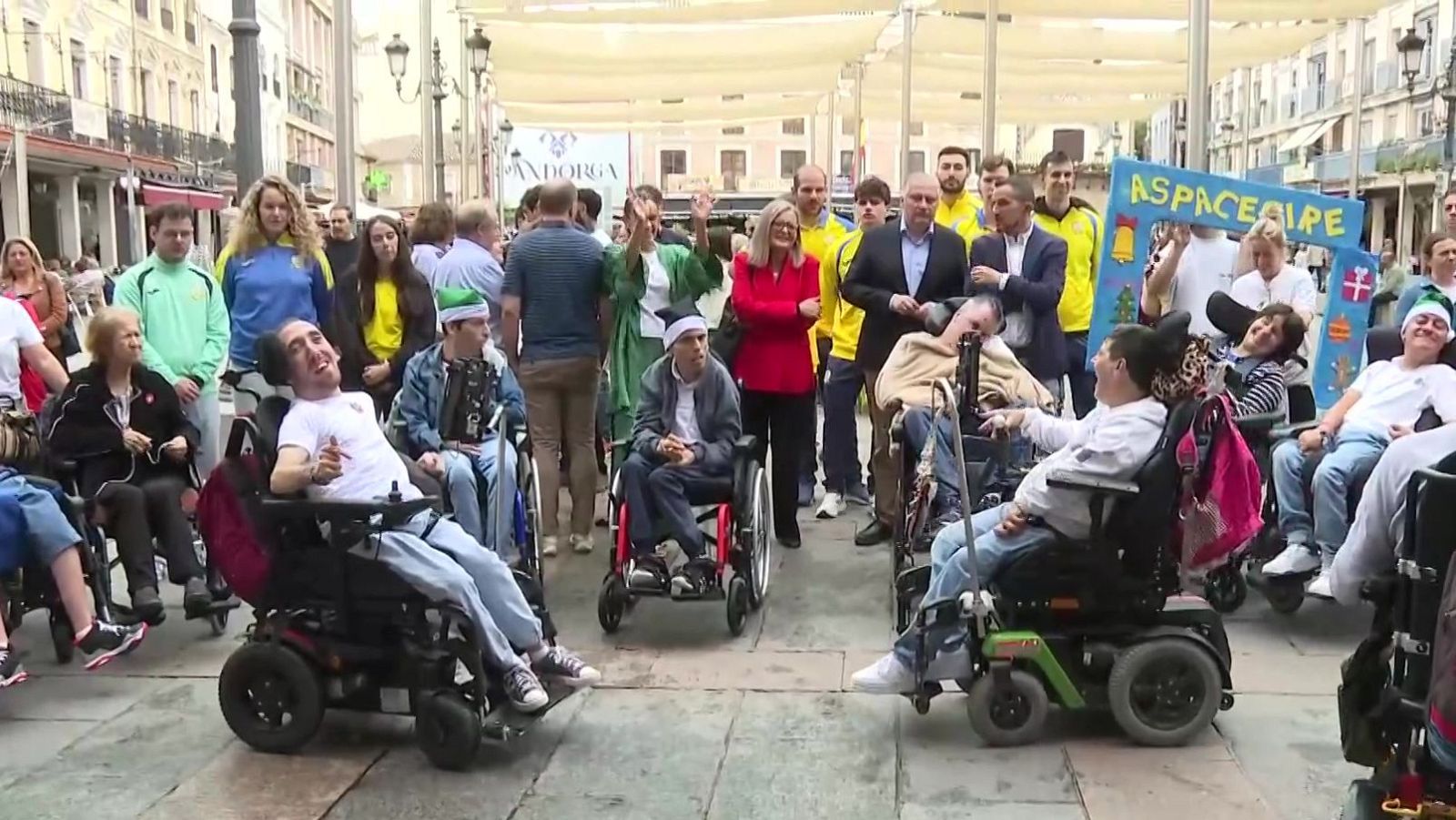 Grupo de personas con parálisis cerebral, familiares y voluntarios celebran al aire libre bajo toldos blancos junto a un cartel de ASPACECIRE.