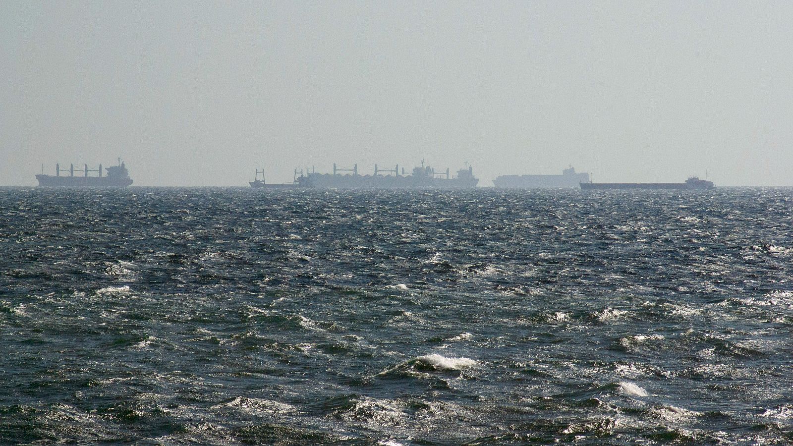 Paisaje marítimo con oleaje en el mar Negro, donde se aprecian varios buques mercantes silueteados en el horizonte bajo un cielo brumoso.