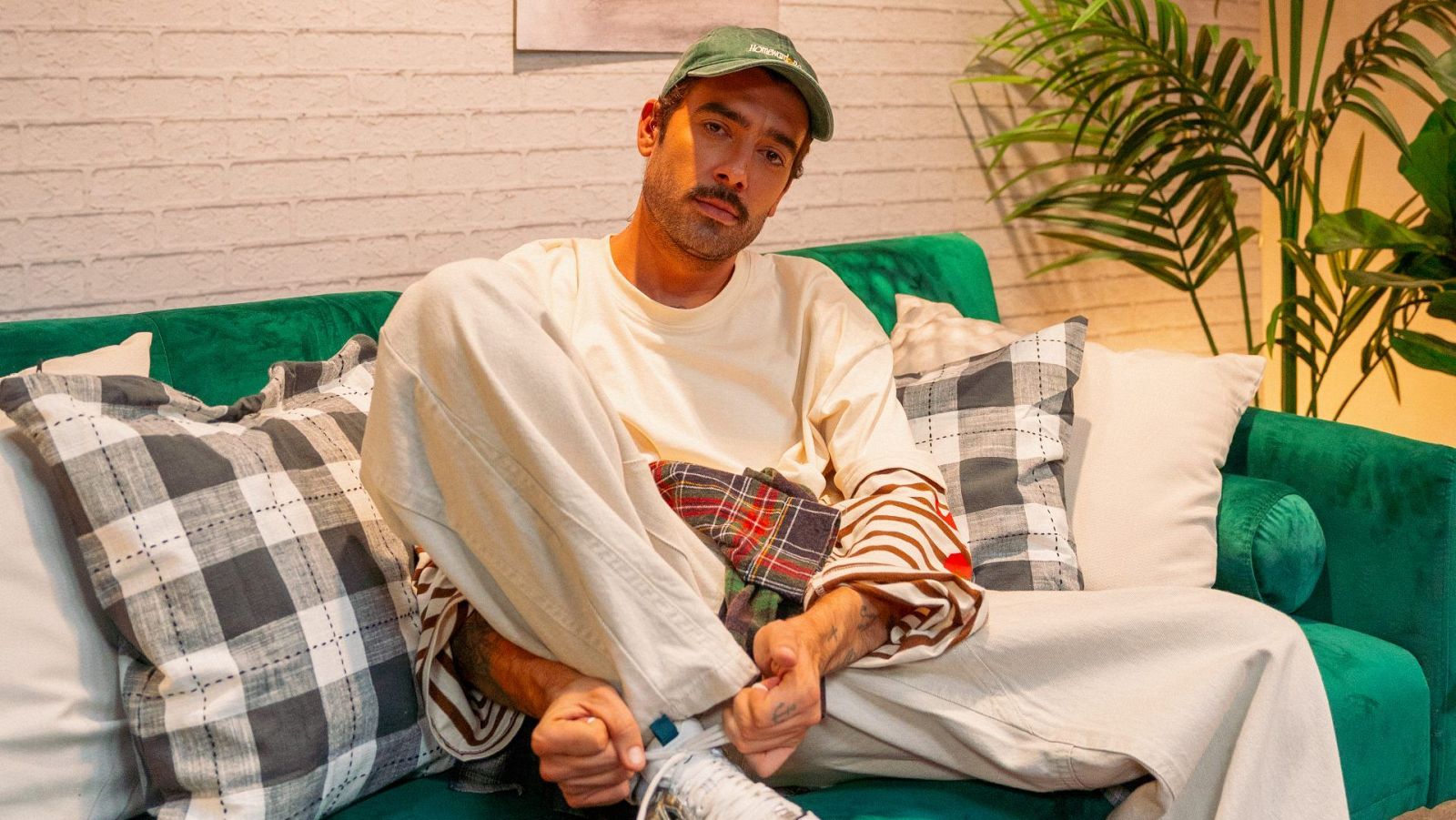 Marc Biarnés posa relajado en un sofá verde con gorra y ropa urbana, mirando a la cámara en un estudio iluminado.