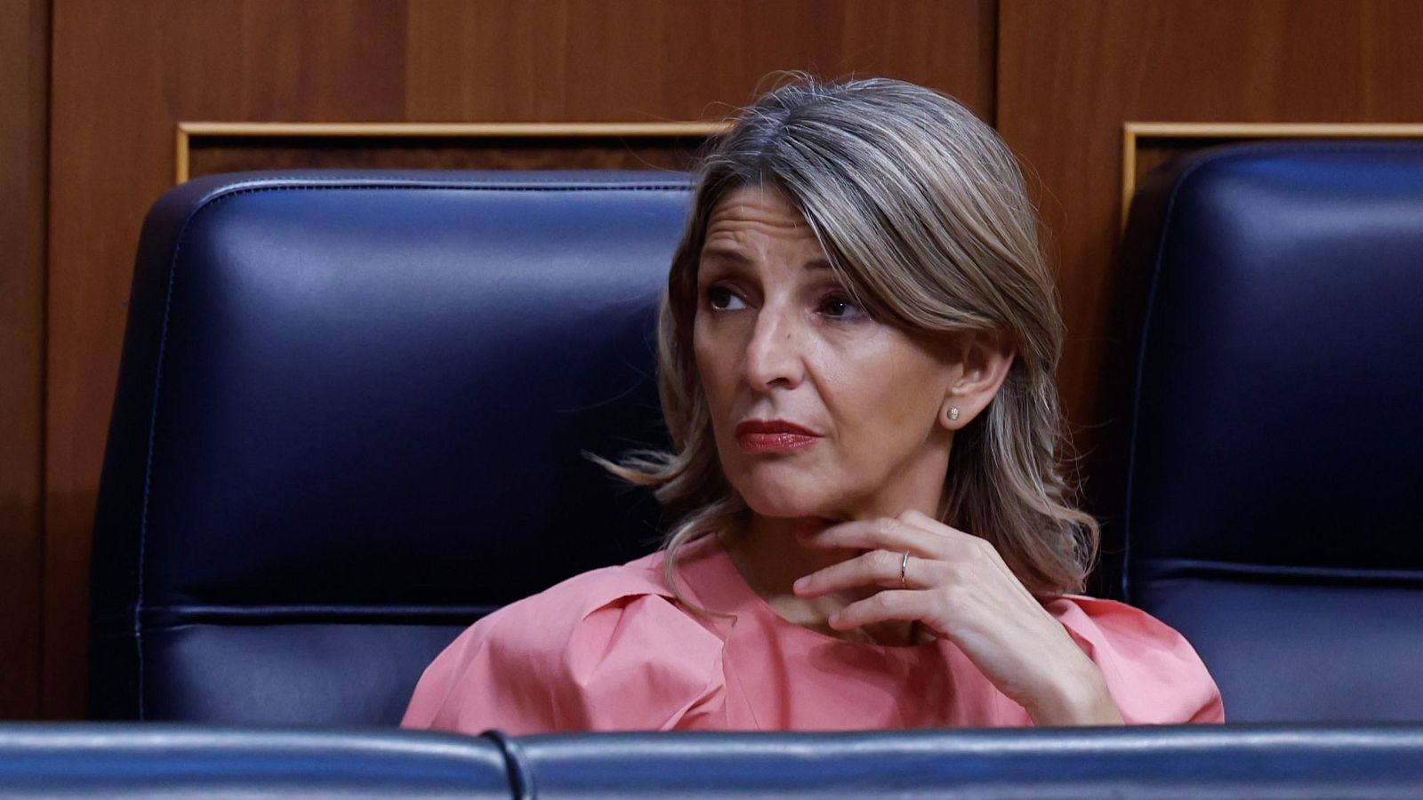 Yolanda Díaz, política española, sentada en el Congreso de los Diputados, con blusa rosa salmón y expresión atenta. Cabello rubio con mechas grises.