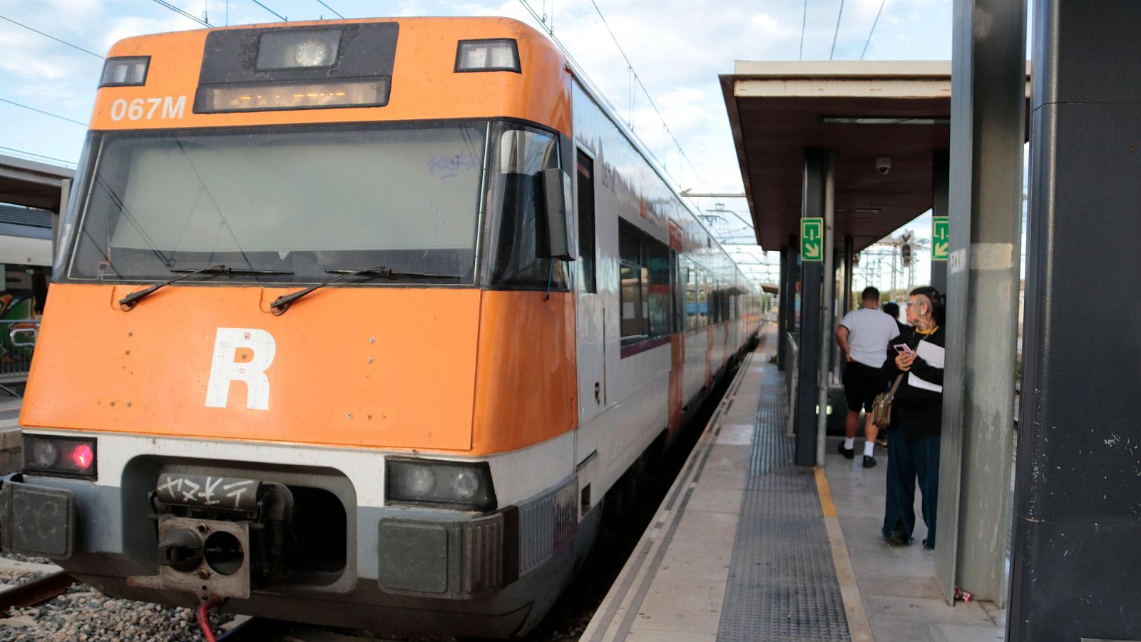 Tren de Rodalies estacionat a l'andana d'una estació amb un passatger mirant el mòbil.